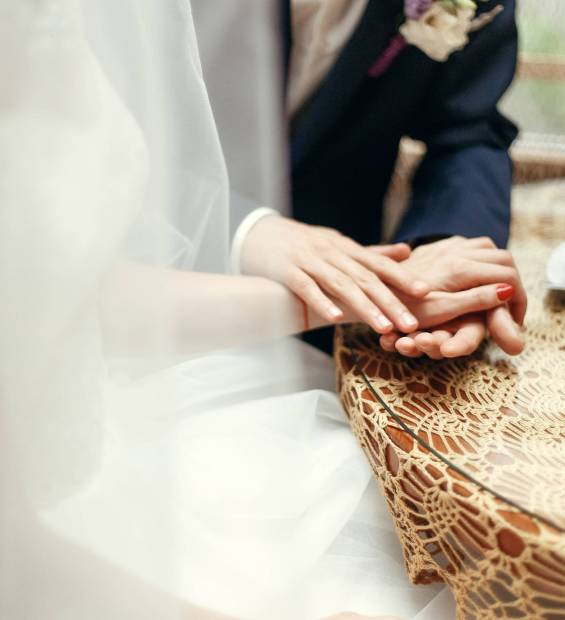 stylish wedding couple holding hands, sitting at wooden vintage table with warm coffee in cups in cafe. happy  bride and groom in dress and suit  hugging